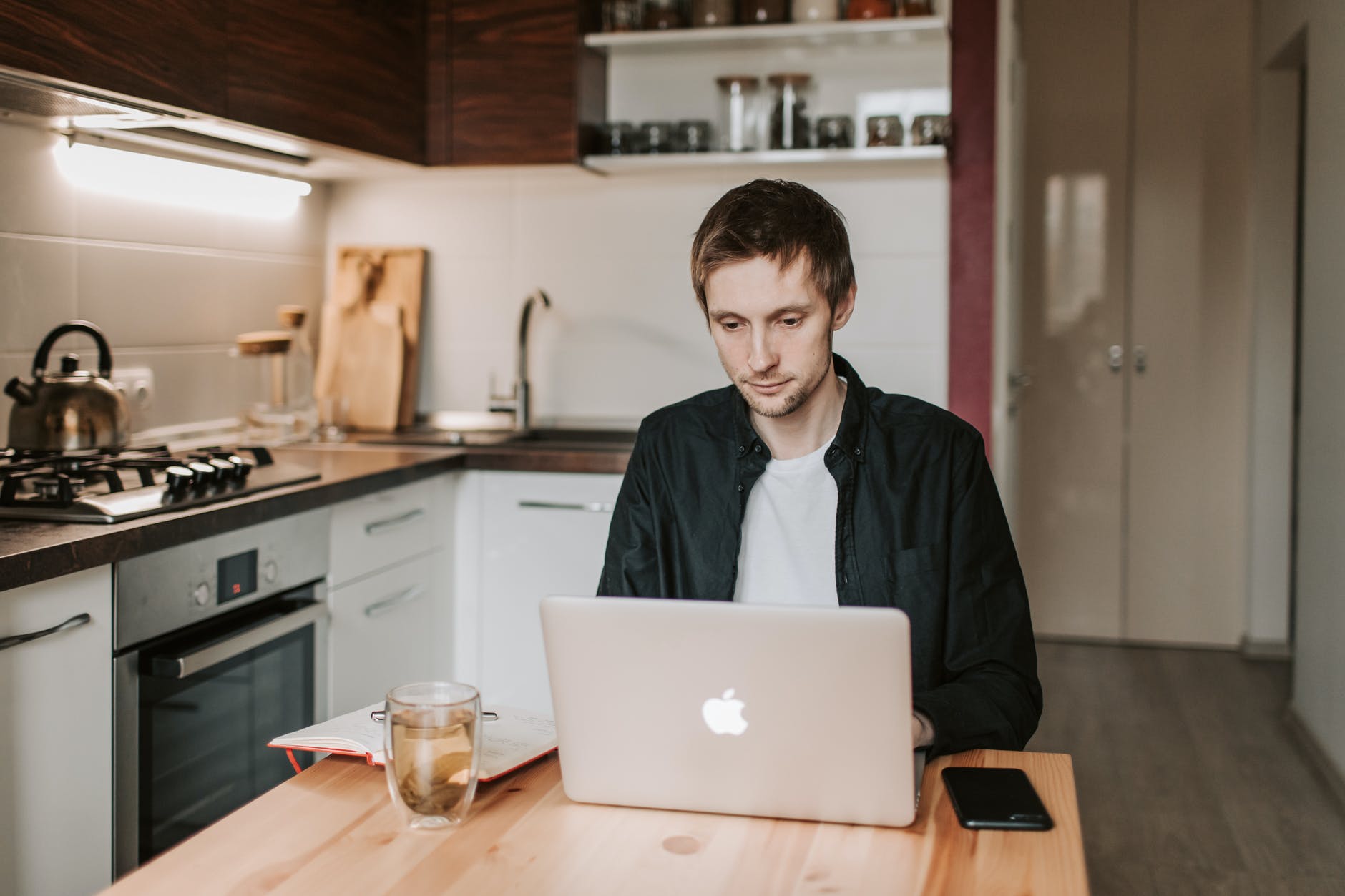 thoughtful male student working on laptop in kitchen at home